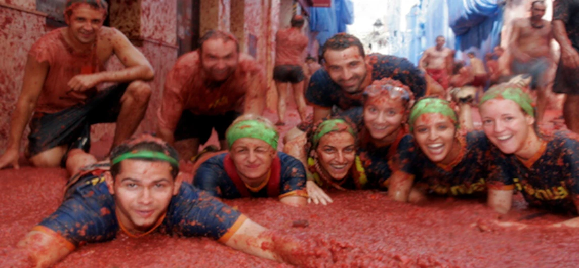 Chicos celebrando tumbados en la calle cubierta de tomates